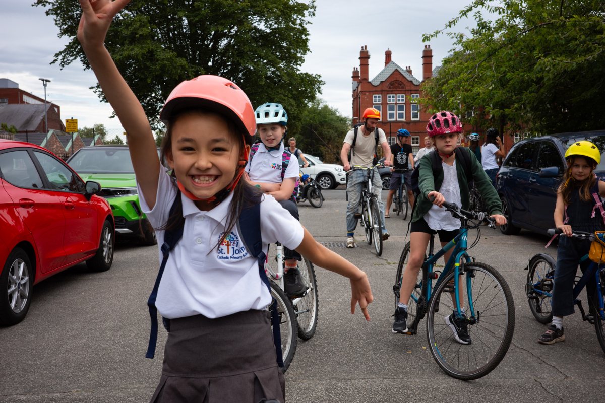 A child waving happily surrounded by a group of children cycling to school together
