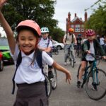 Child smiling in school uniformand jumping with other children behind on bikes